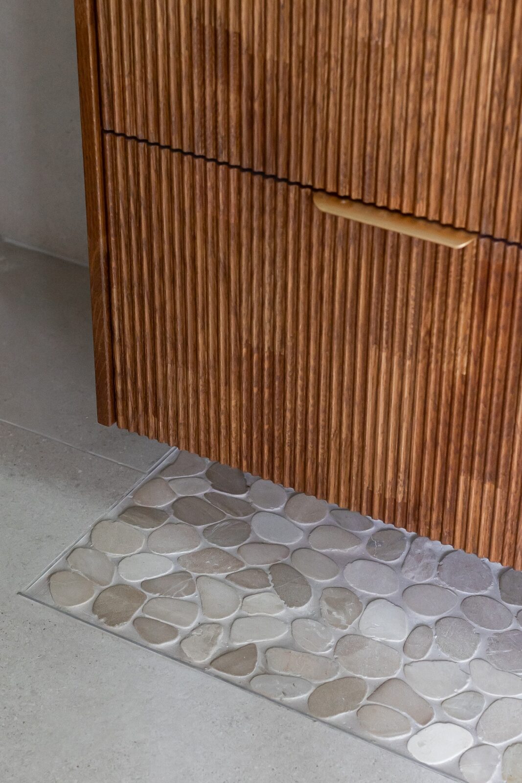 Rishon LeZion bathroom detail with fluted wood vanity and pebble stone floor