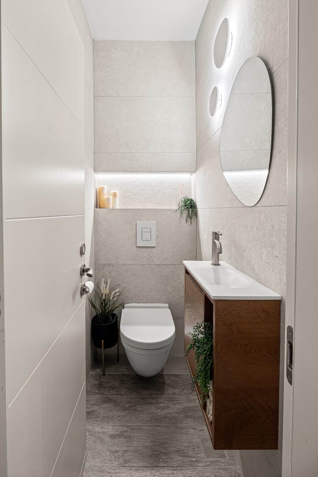 Rishon LeZion powder room with floating wood vanity, oval mirror and recessed lit niche