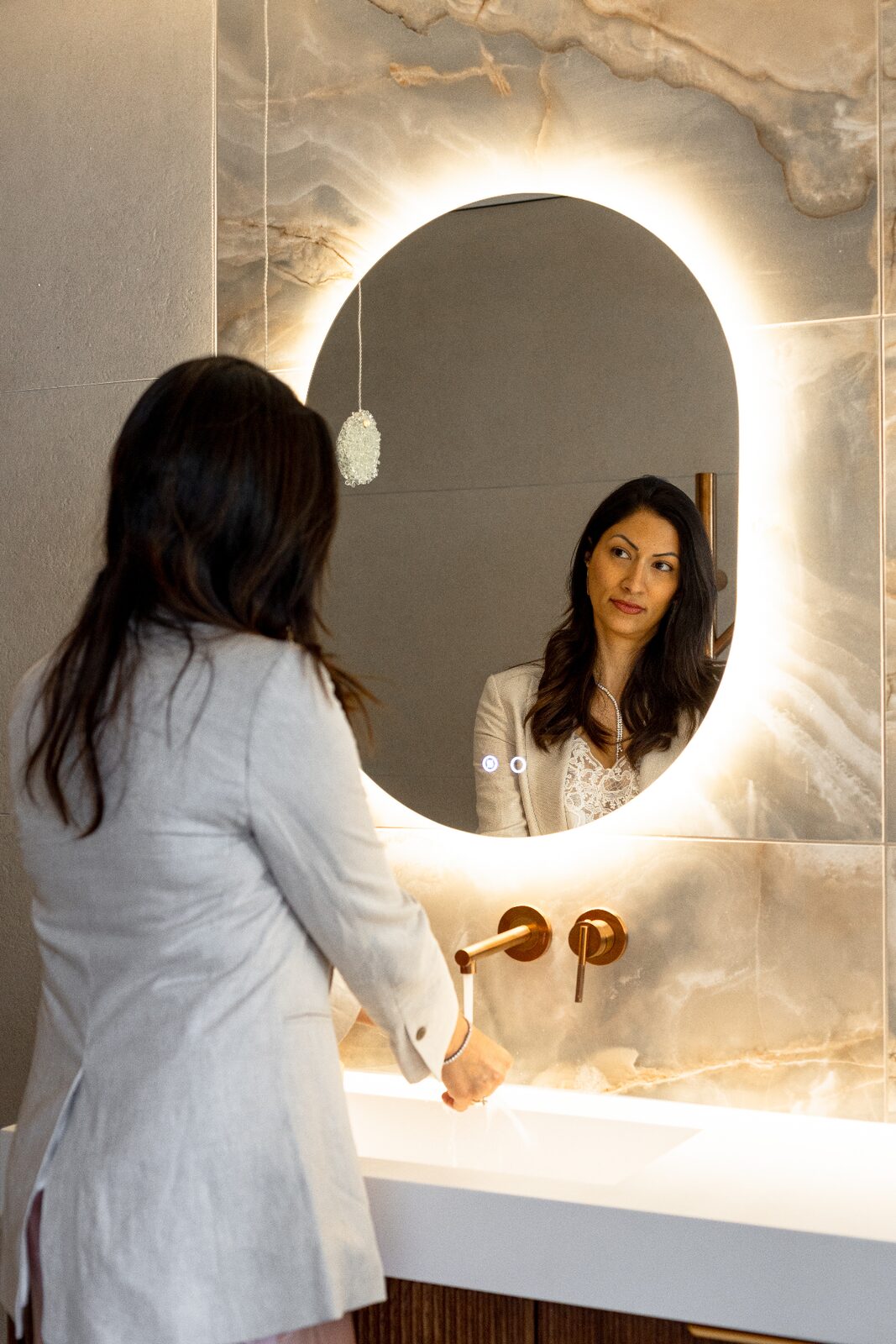Rishon LeZion bathroom with backlit oval mirror and onyx stone wall
