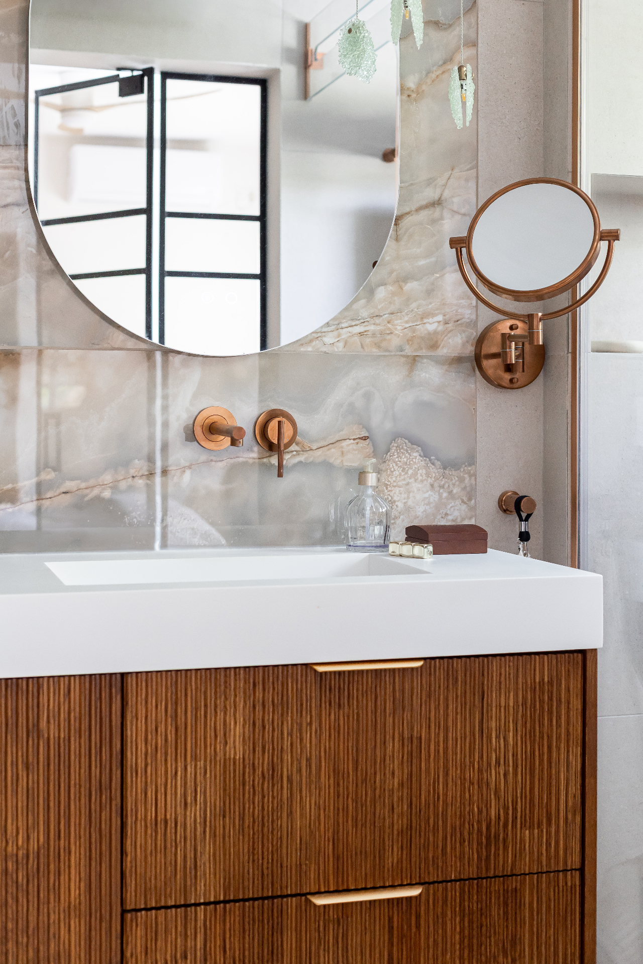 Rishon LeZion bathroom vanity detail with fluted wood cabinet, round mirror and onyx wall