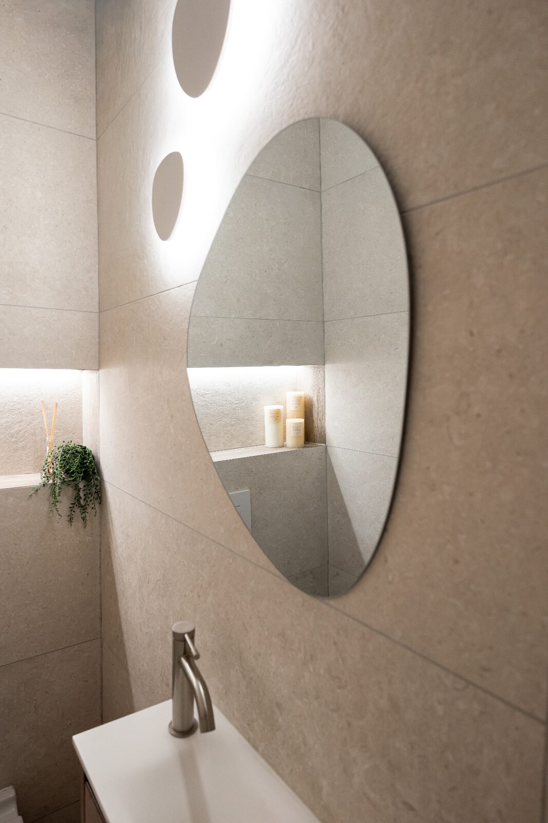 Rishon LeZion powder room detail with organic mirror and backlit stone niche