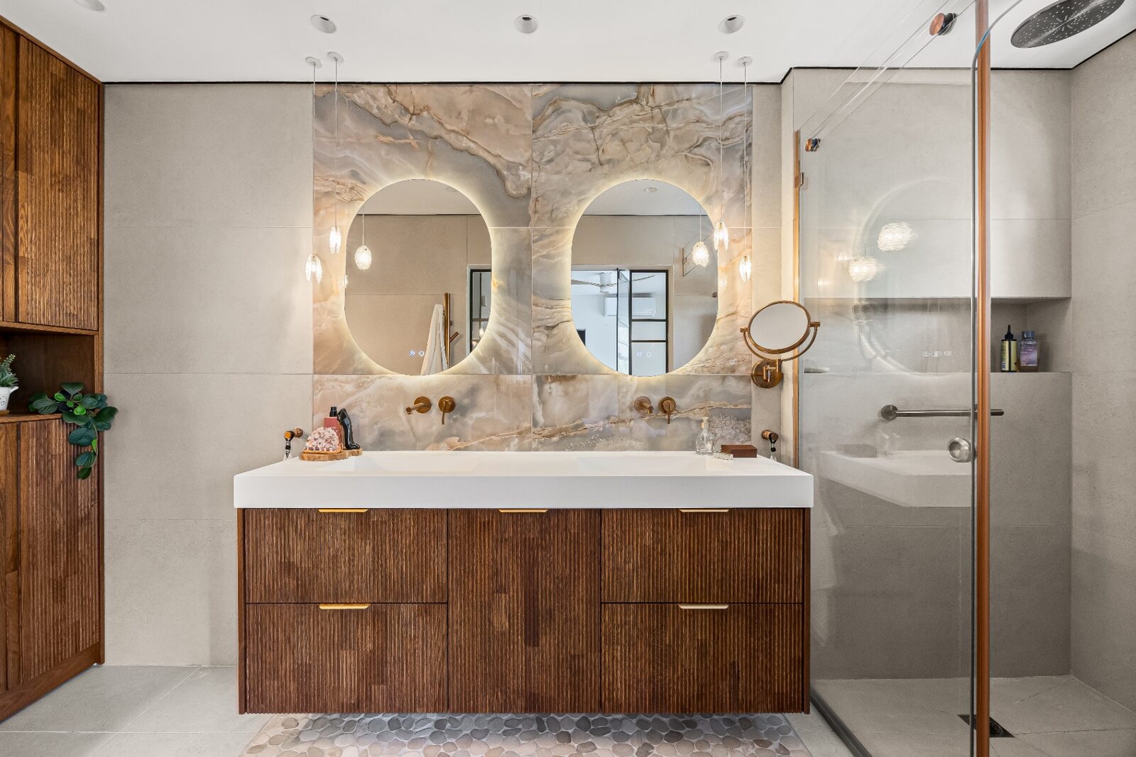 Rishon LeZion master bathroom vanity with twin round mirrors, onyx wall and fluted wood cabinetry